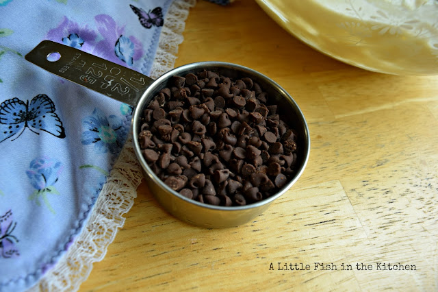 A metal one cup measuring cup holds a half measure of mini chocolate chips.  