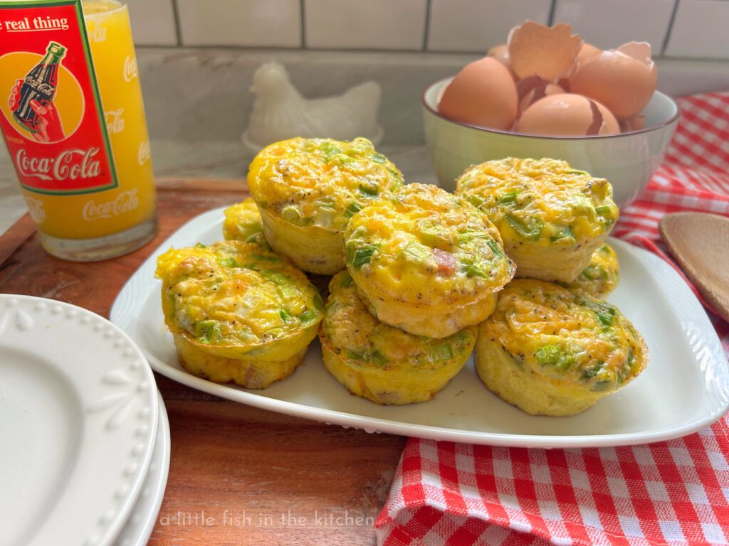 Denver omelette egg muffins filled with diced ham, red and green bell peppers, onions, and melted cheddar cheese, arranged on a rectangular white plate. The fluffy, protein-packed egg muffins have lightly browned tops with colorful vegetables peeking through, making for a hearty and inviting make-ahead breakfast.