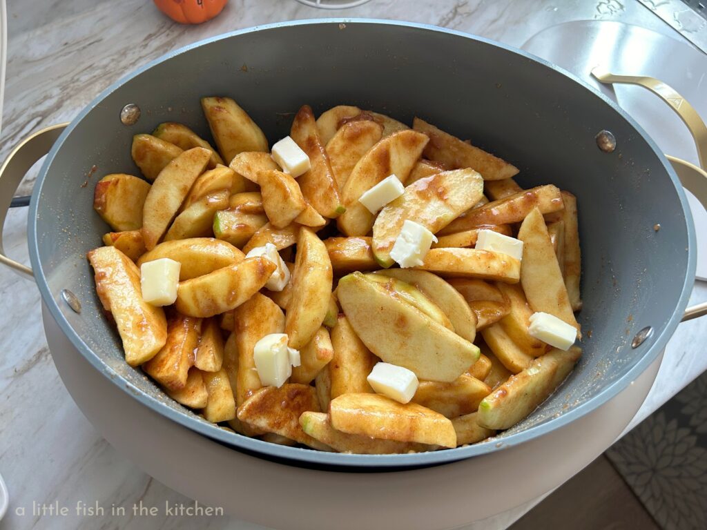 Crispy, fresh apple slices are coated in a buttery pumpkin spice and sugar mixture in a dutch oven. The seasoned fresh apples are dotted with cubes of butter just before cooking begins. 