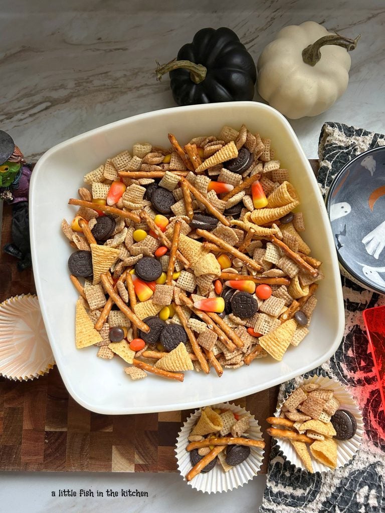 A vintage yellow square serving bowl is filled with an delicious batch of no bake fall snack mix. In the bowl, corn chips, candy corn, pretzel sticks, mini Oreo cookies, and candy pieces are all visible. 
