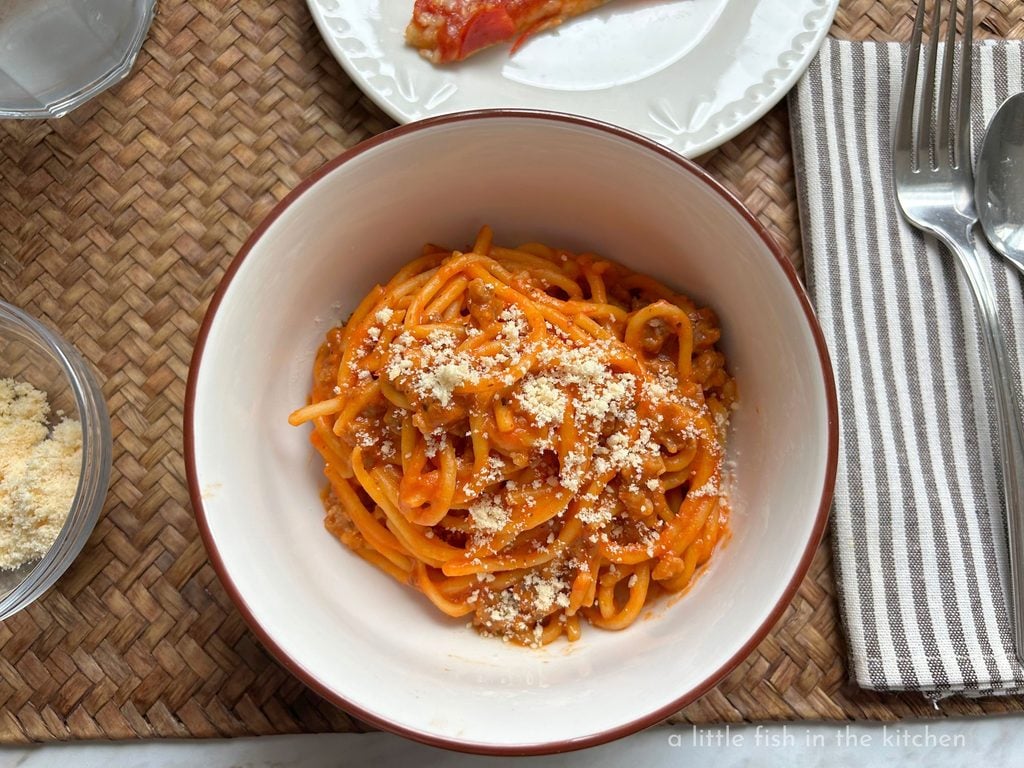 A generous serving easy creamy spaghetti is in a white ceramic bowl with a brown rim. Bits of tender ground meat are visible mixed in the rich sauce cooked pasta. A generous sprinkle of grated parmesan cheese is sprinkled on top of the dish making it look extra flavorful and delicious. 